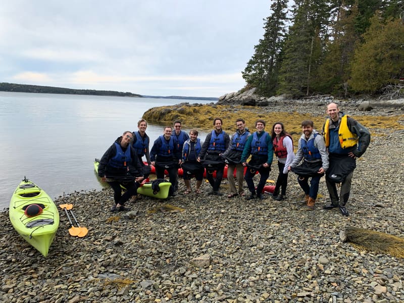 Churchman Lab group portrait on a rocky Maine beach beside the kayaks